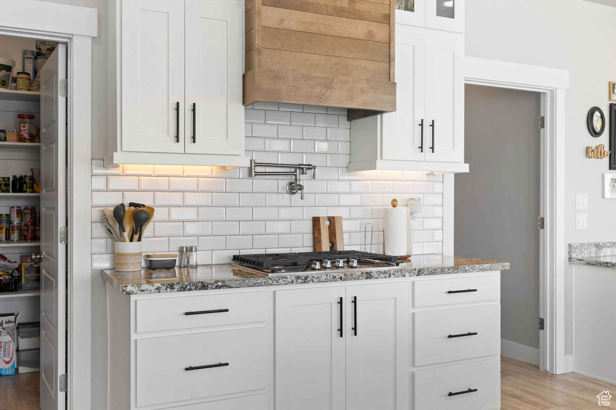Kitchen featuring custom exhaust hood, backsplash, light wood-type flooring, white cabinetry, and light stone countertops