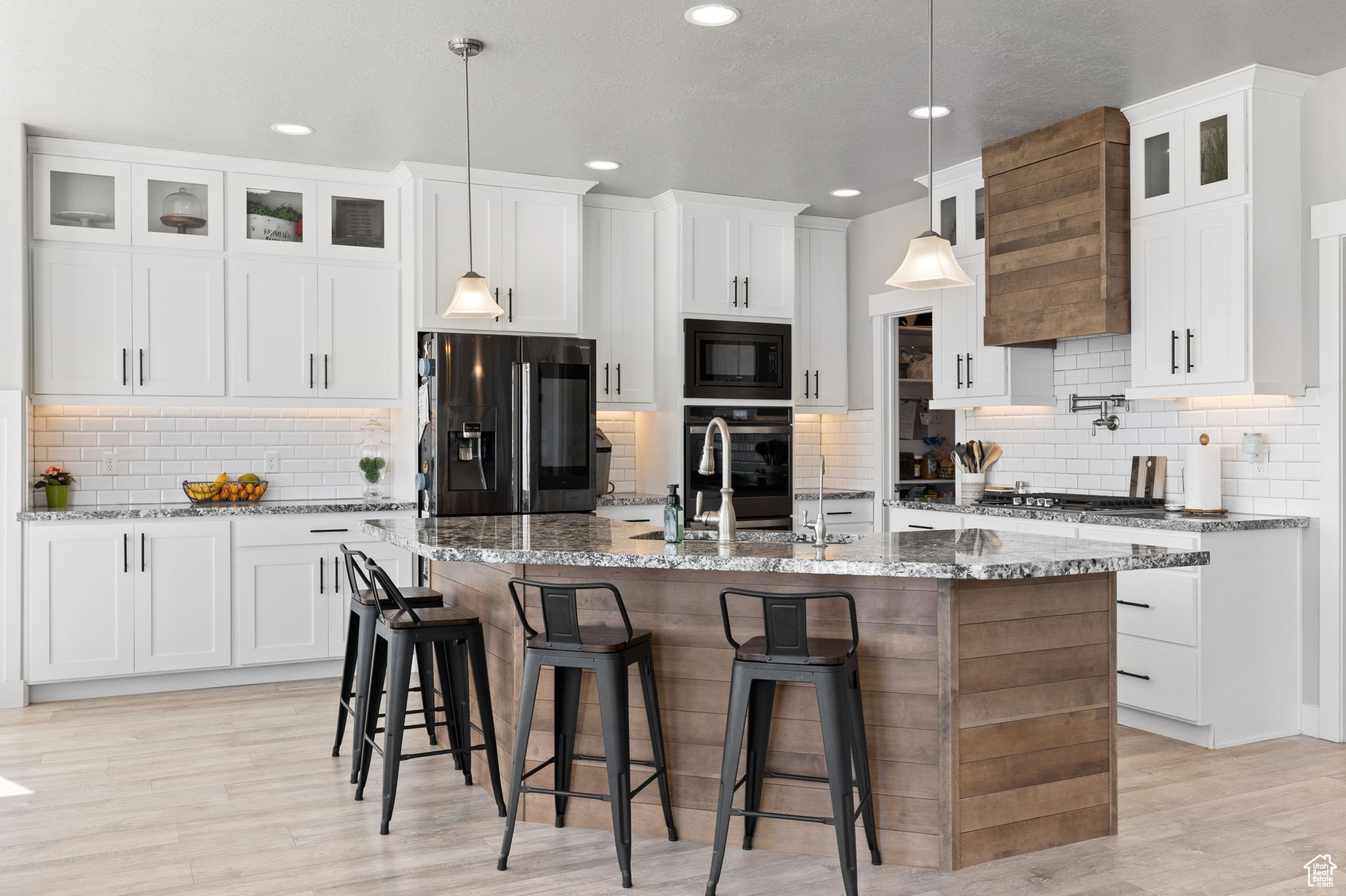 Kitchen featuring decorative light fixtures, black appliances, and an island with sink