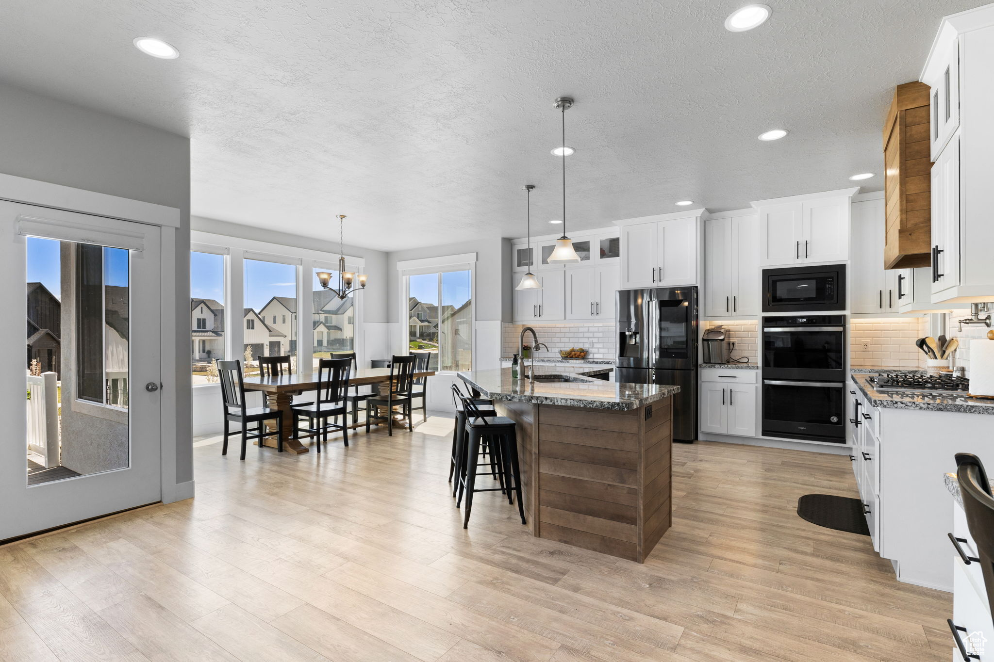 Kitchen with decorative light fixtures, white cabinets, light hardwood / wood-style flooring, black appliances, and an island with sink