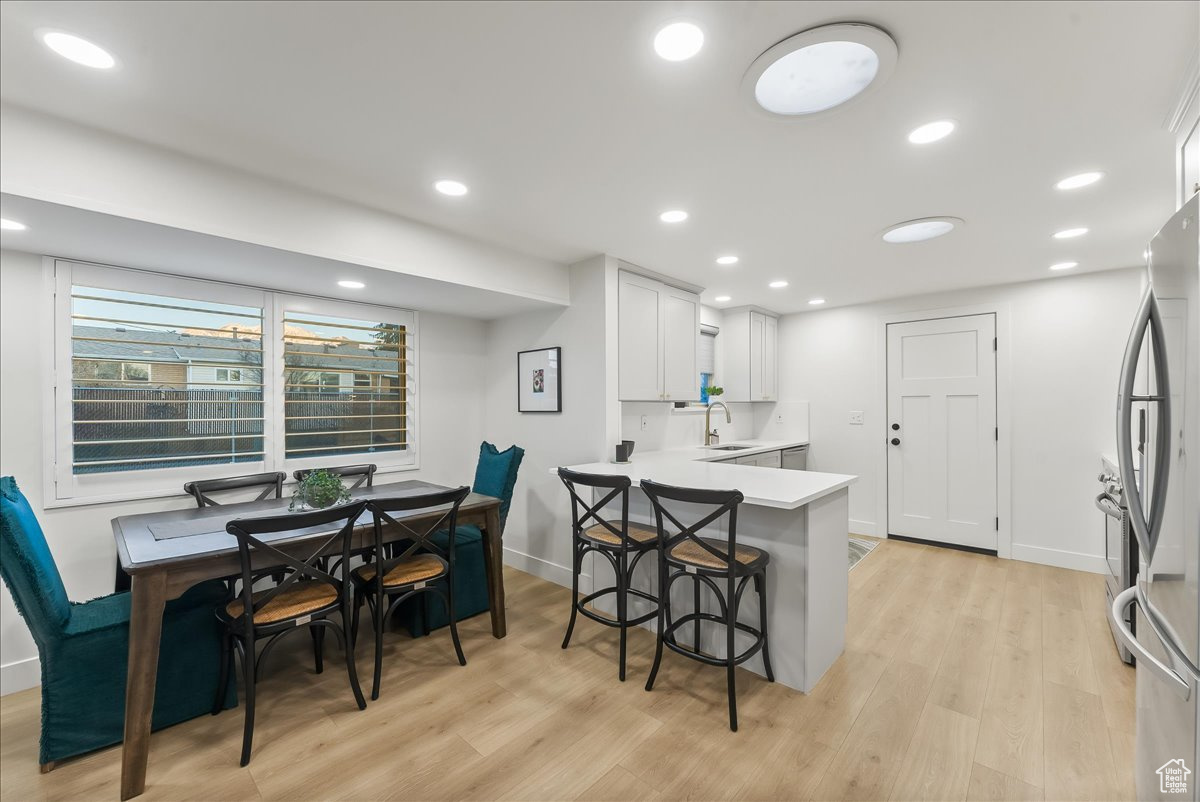 Kitchen featuring kitchen peninsula, light hardwood / wood-style flooring, white cabinetry, stainless steel fridge, and sink