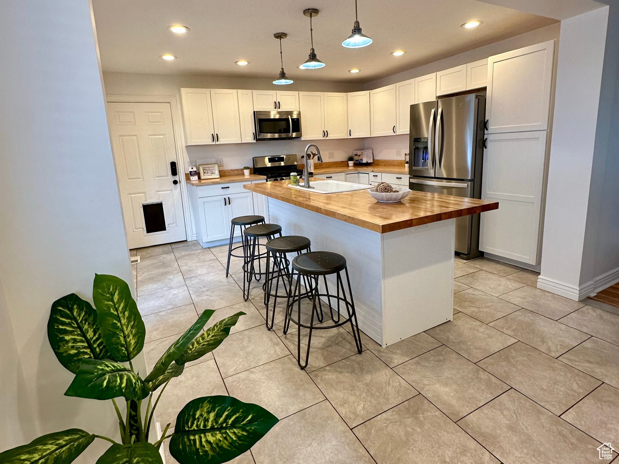 Kitchen featuring decorative light fixtures, appliances with stainless steel finishes, a center island with sink, white cabinets, and wooden counters