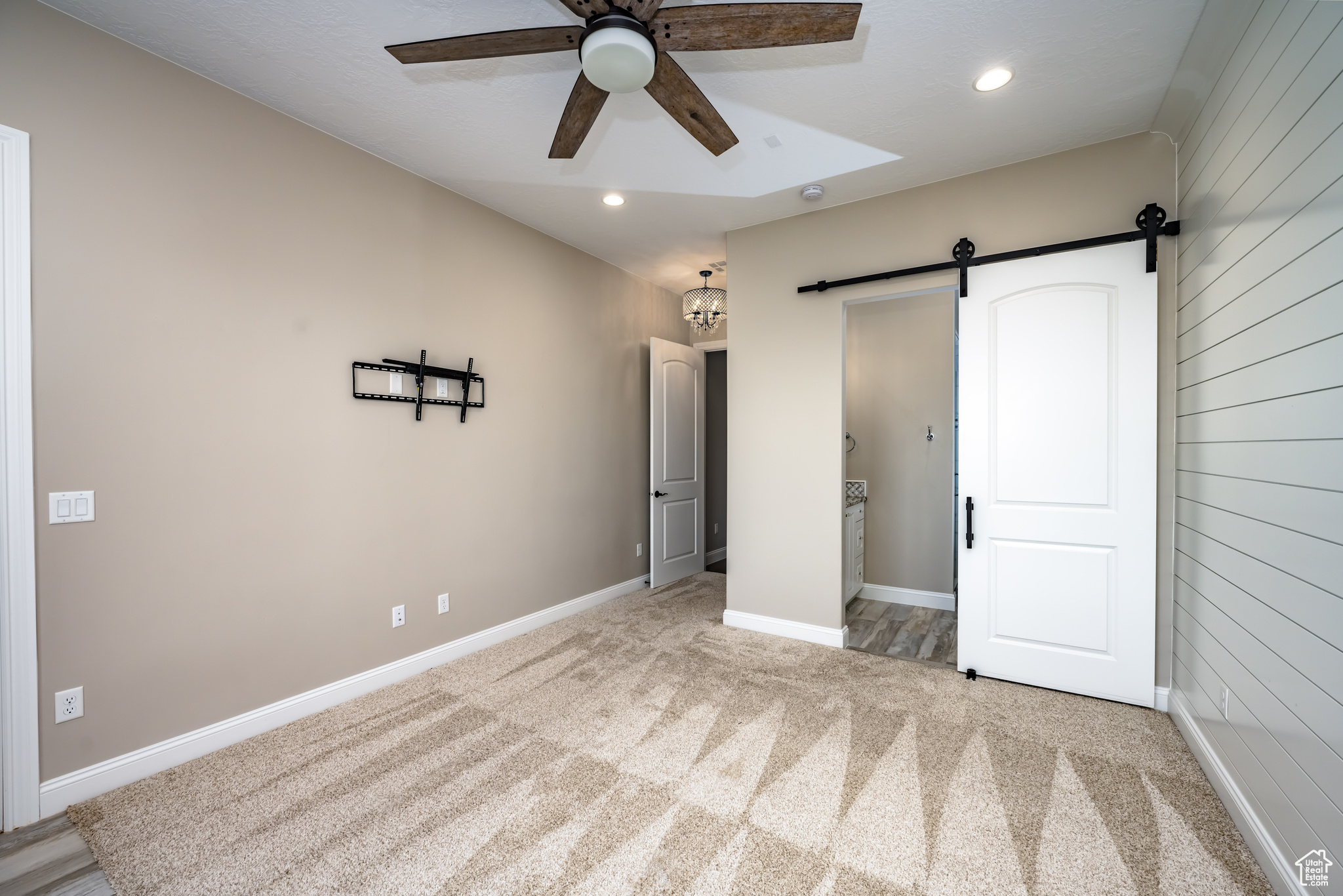 Unfurnished bedroom with light carpet, ceiling fan, and a barn door