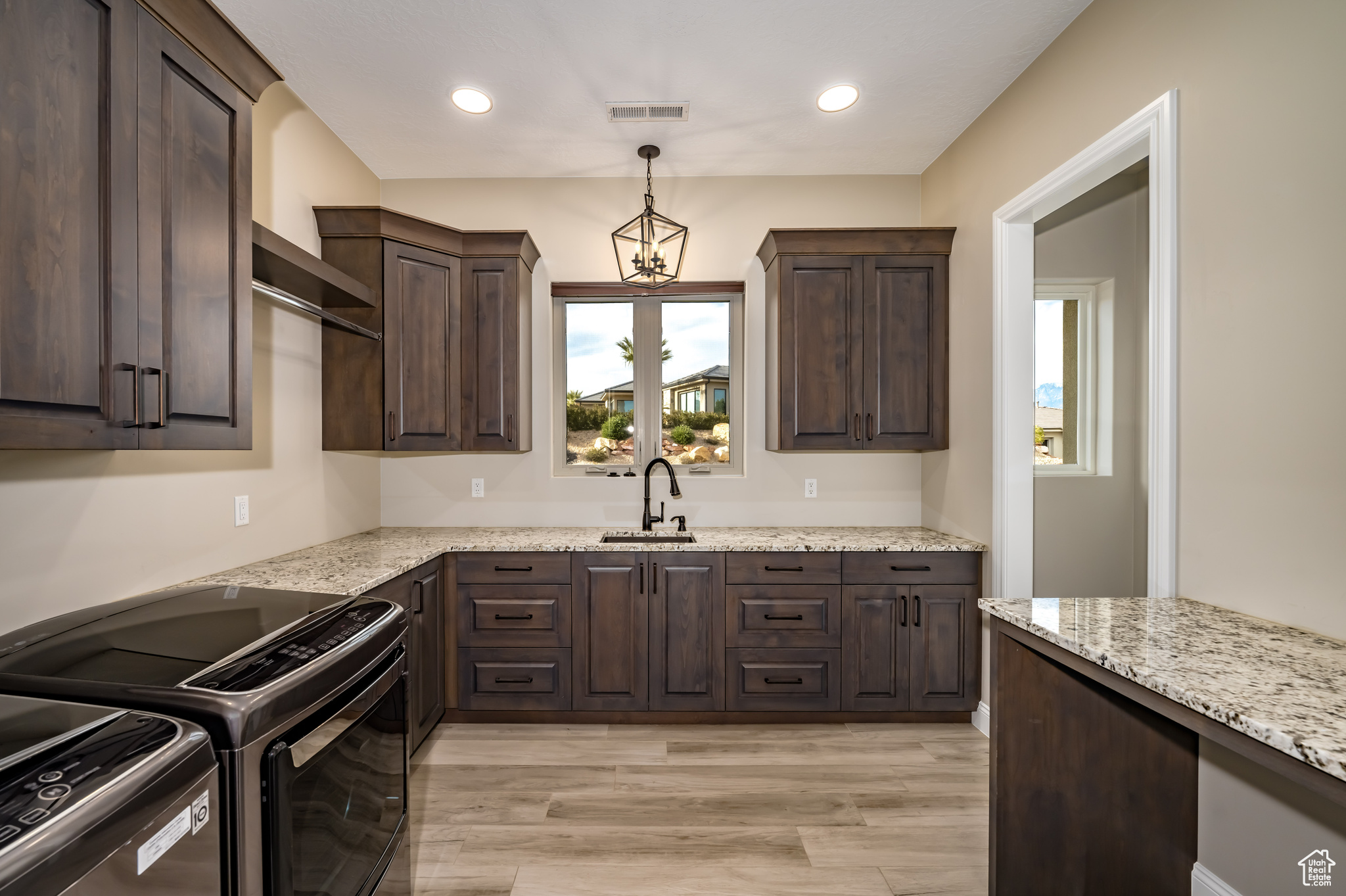 Kitchen featuring light hardwood / wood-style floors, dark brown cabinets, sink, and light stone countertops