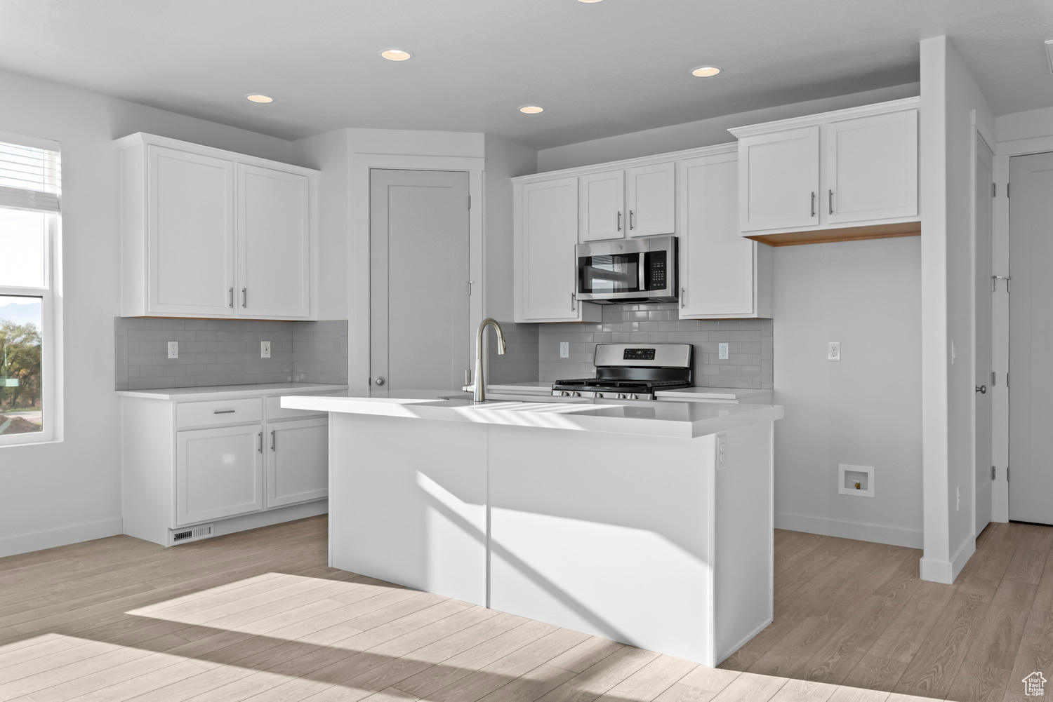 Kitchen with appliances with stainless steel finishes, white cabinets, and an island with sink