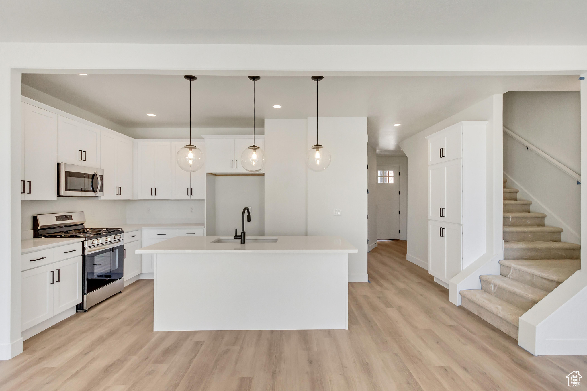 Kitchen with pendant lighting, light hardwood / wood-style flooring, stainless steel appliances, and white cabinets