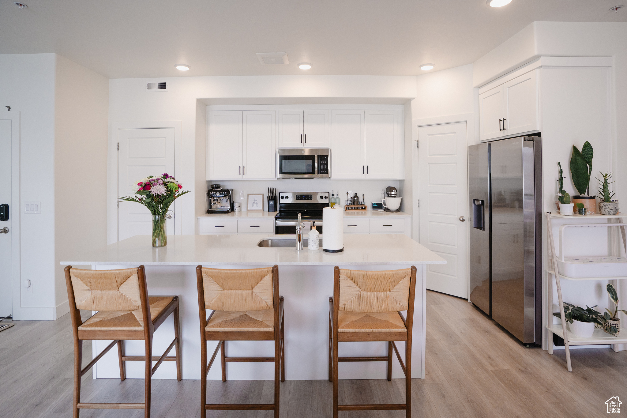 Kitchen featuring appliances with stainless steel finishes, a center island with sink, white cabinetry, a kitchen breakfast bar, and light wood-type flooring