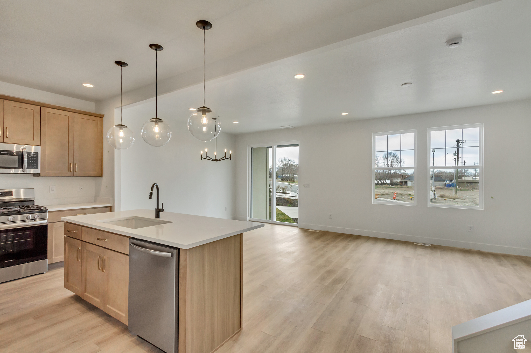 Kitchen featuring decorative light fixtures, stainless steel appliances, sink, light hardwood / wood-style floors, and an island with sink
