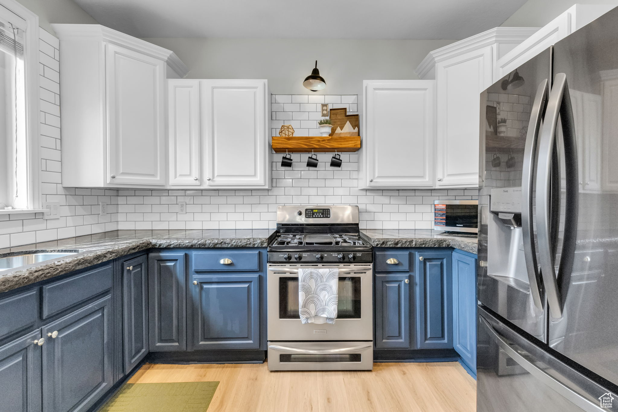 Kitchen with appliances with stainless steel finishes, tasteful backsplash, light wood-type flooring, and white cabinetry