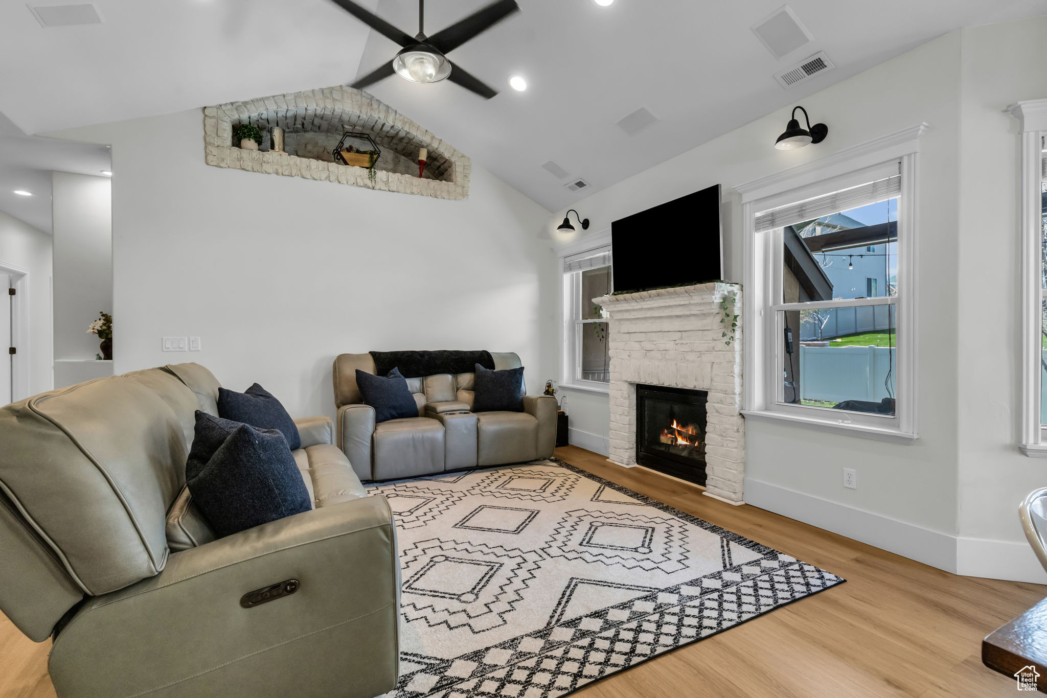 Living room with ceiling fan, a fireplace, vaulted ceiling, and light hardwood / wood-style floors