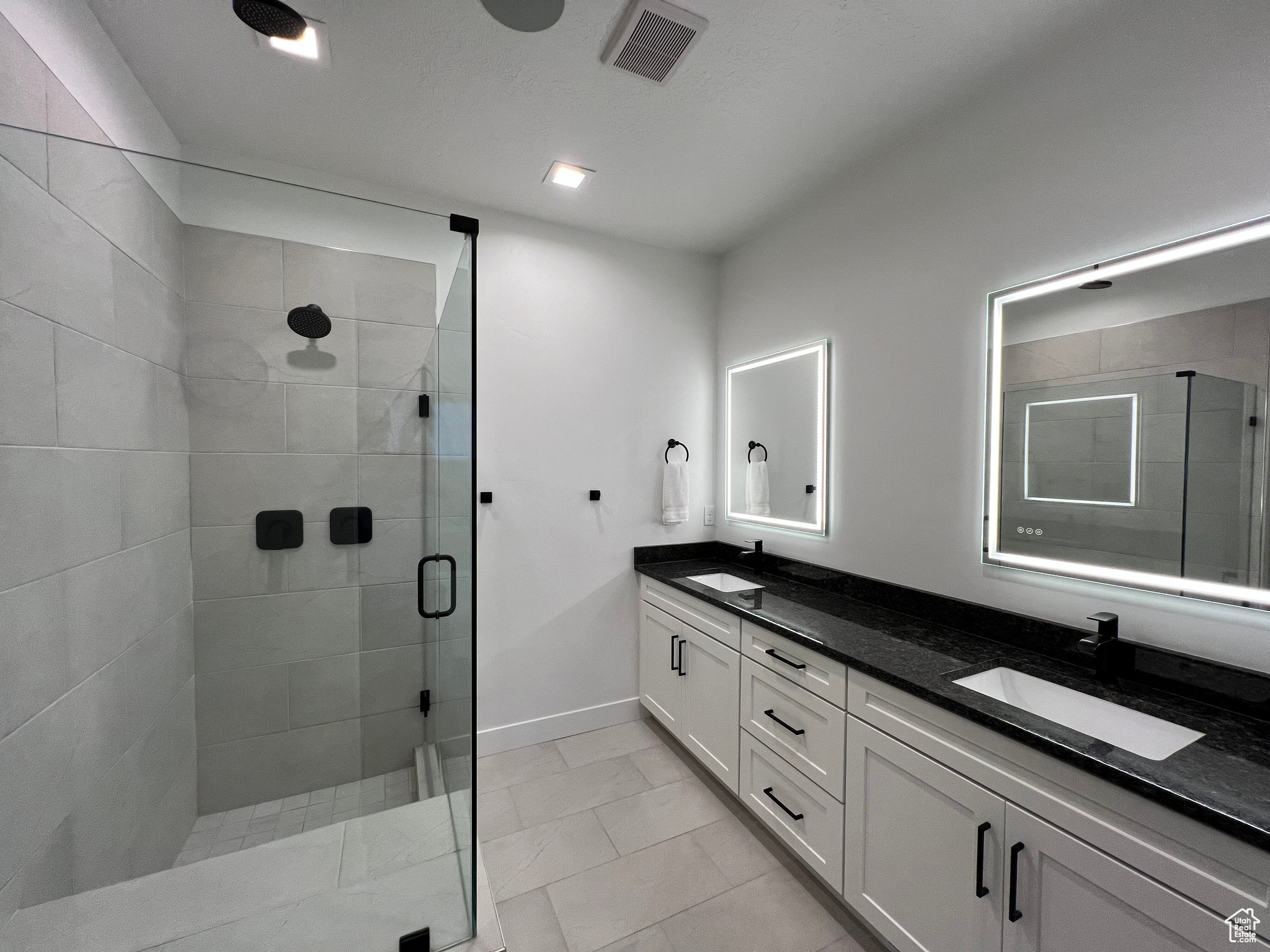 Primary ensuite bathroom with double vanity, lighted mirrors, and spacious shower