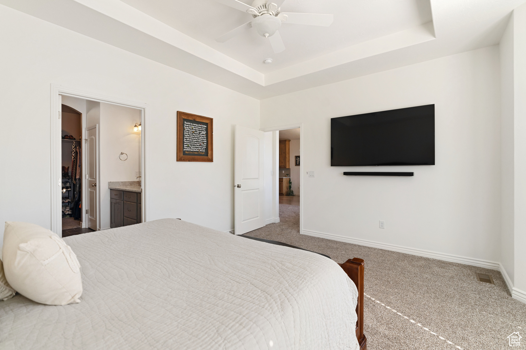 Carpeted bedroom featuring ceiling fan, ensuite bath, and a tray ceiling
