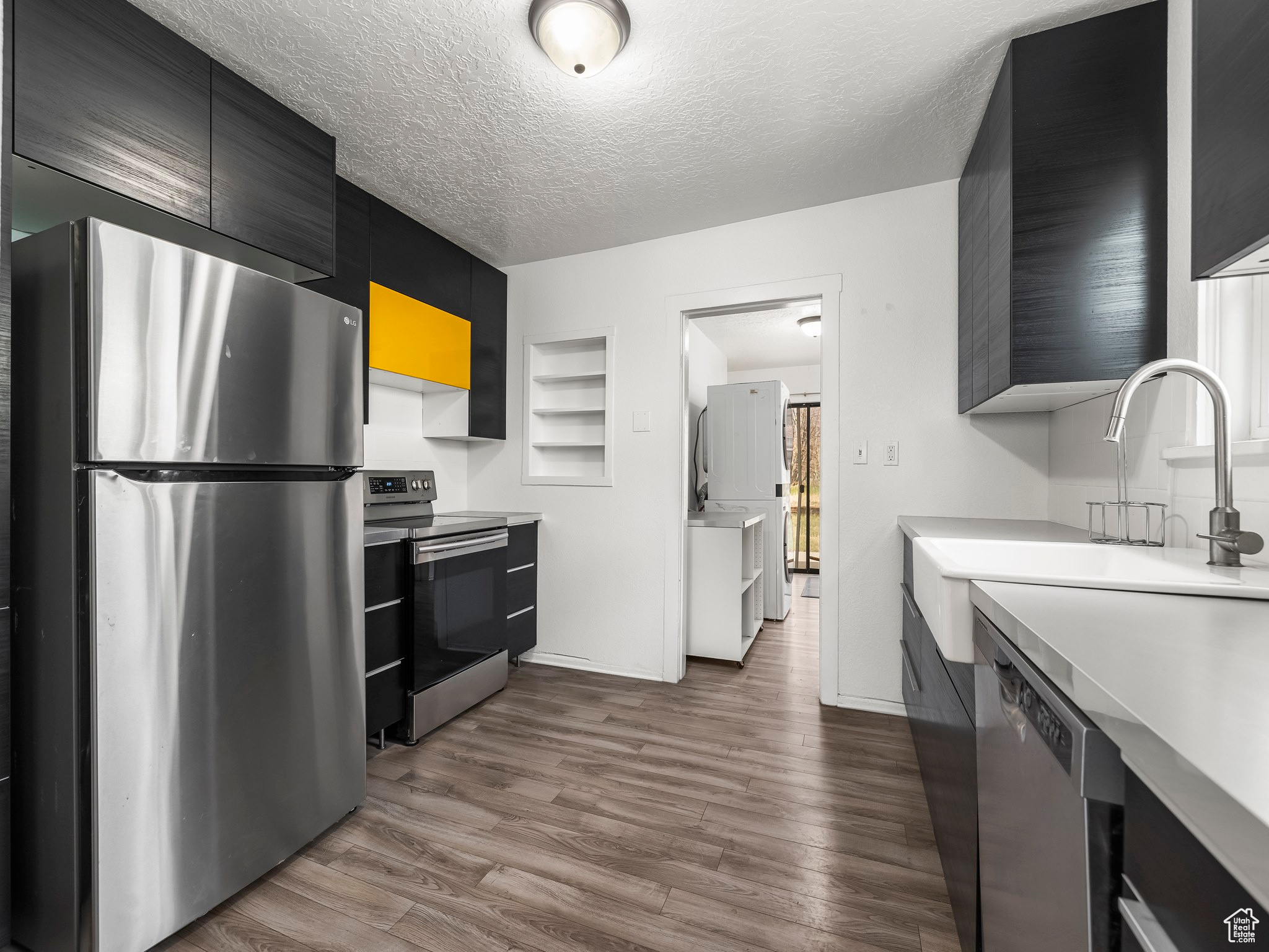 Kitchen with built in features, stainless steel appliances, wood-type flooring, a textured ceiling, and sink