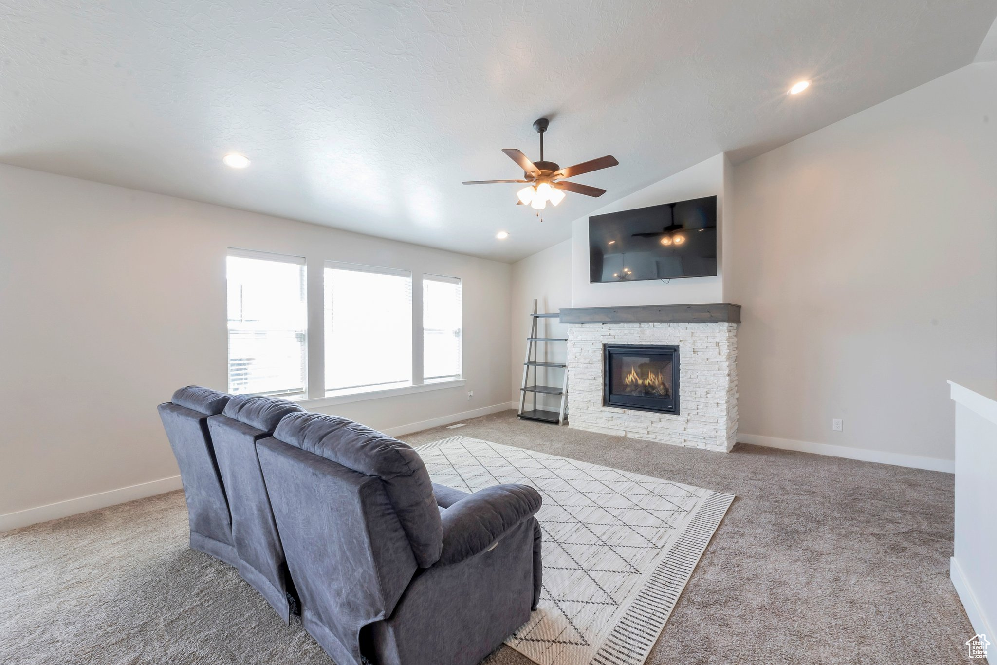Living room featuring ceiling fan, light carpet, a fireplace, and lofted ceiling