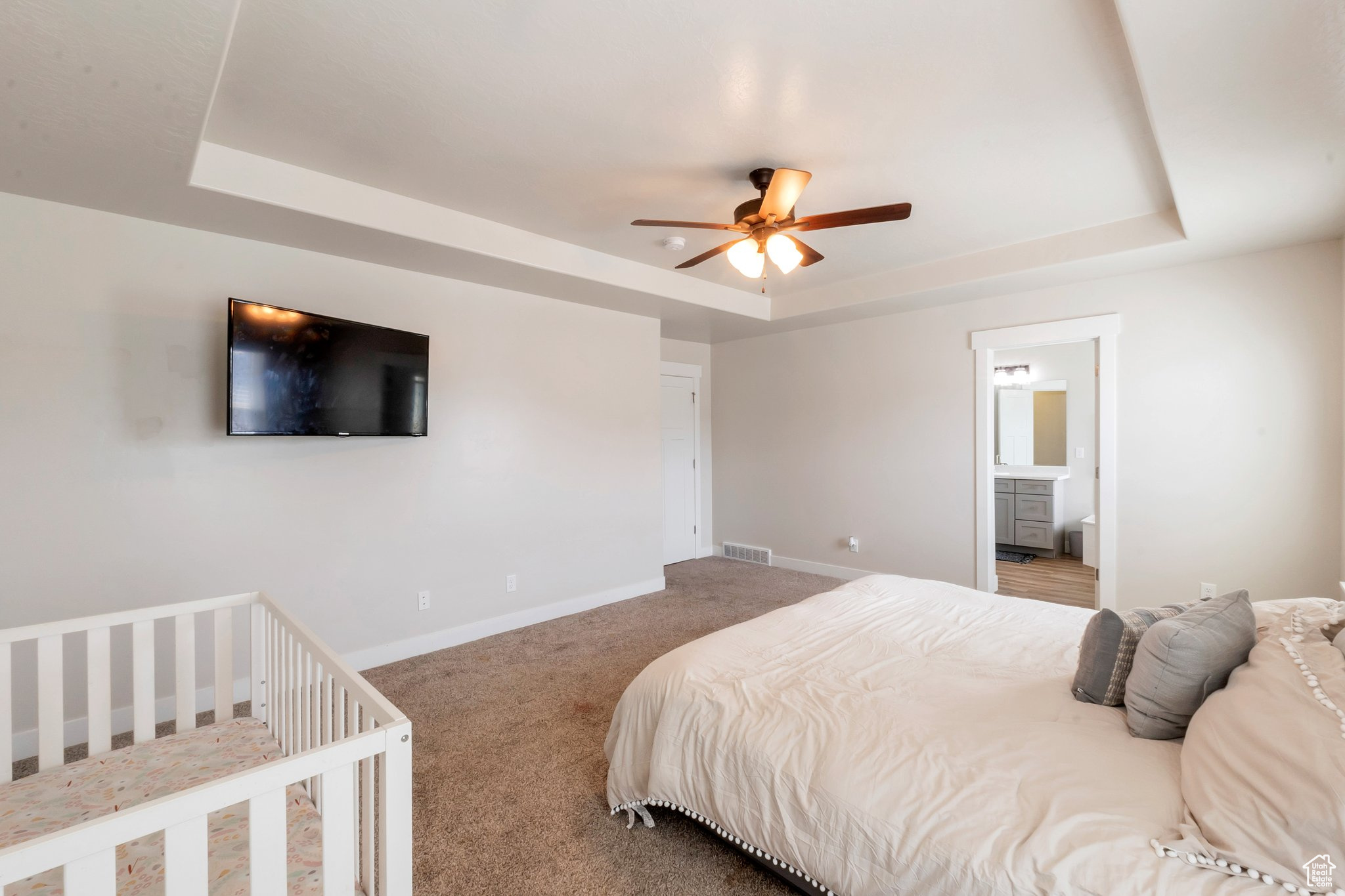 Carpeted bedroom featuring ensuite bathroom, ceiling fan, and a tray ceiling