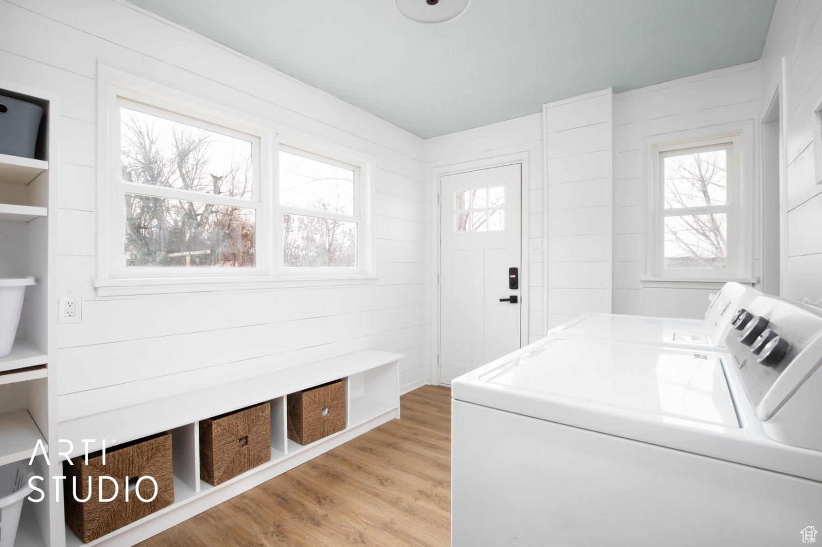 Laundry area with shiplap wall, wood-style LVP floors, built in bench and tower storage and washer and dryer