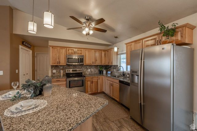 Kitchen with light stone counters, appliances with stainless steel finishes, ceiling fan, hanging light fixtures, and vaulted ceiling