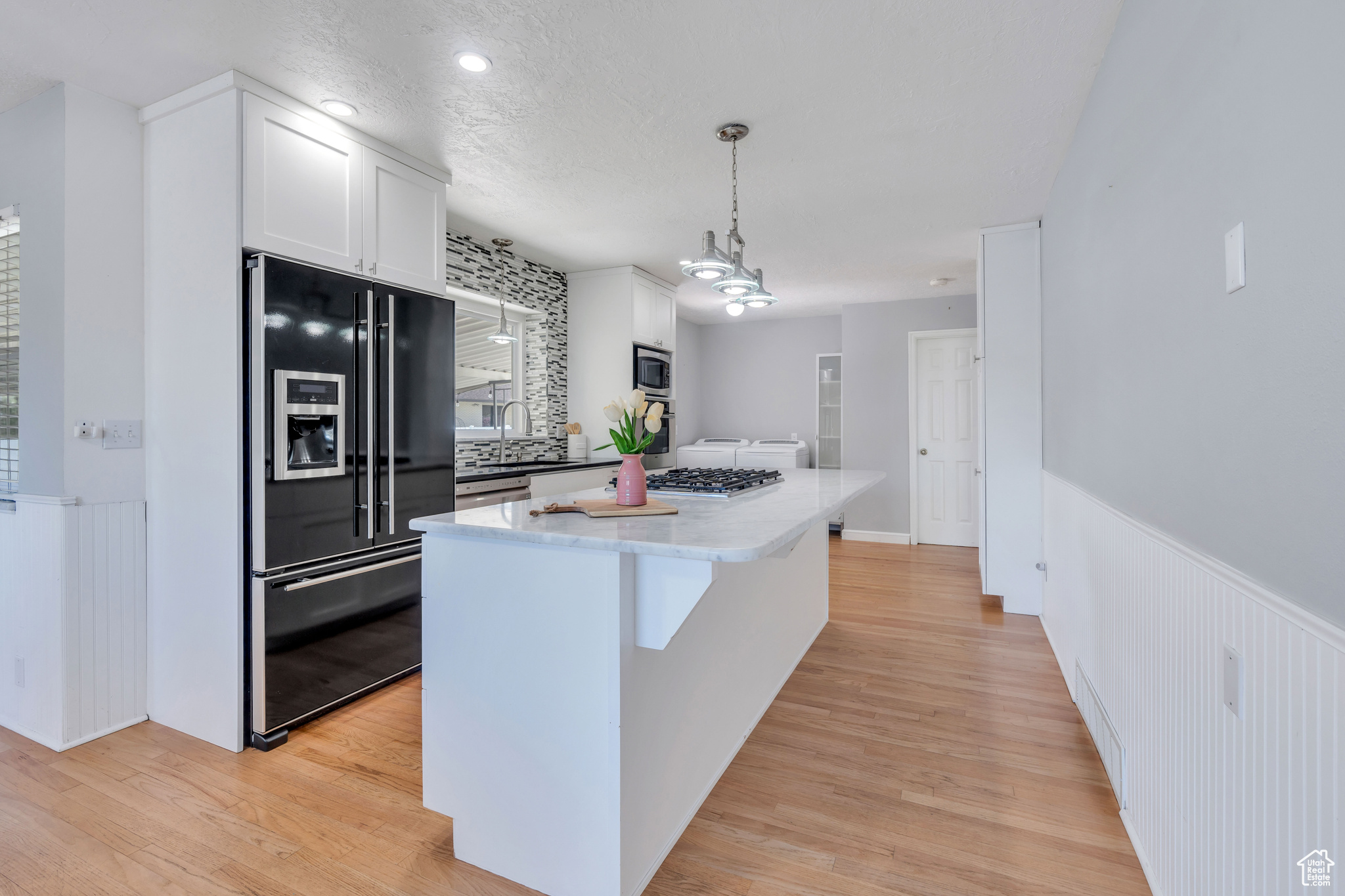 Kitchen featuring white cabinets, light hardwood / wood-style flooring, stainless steel appliances, and decorative light fixtures