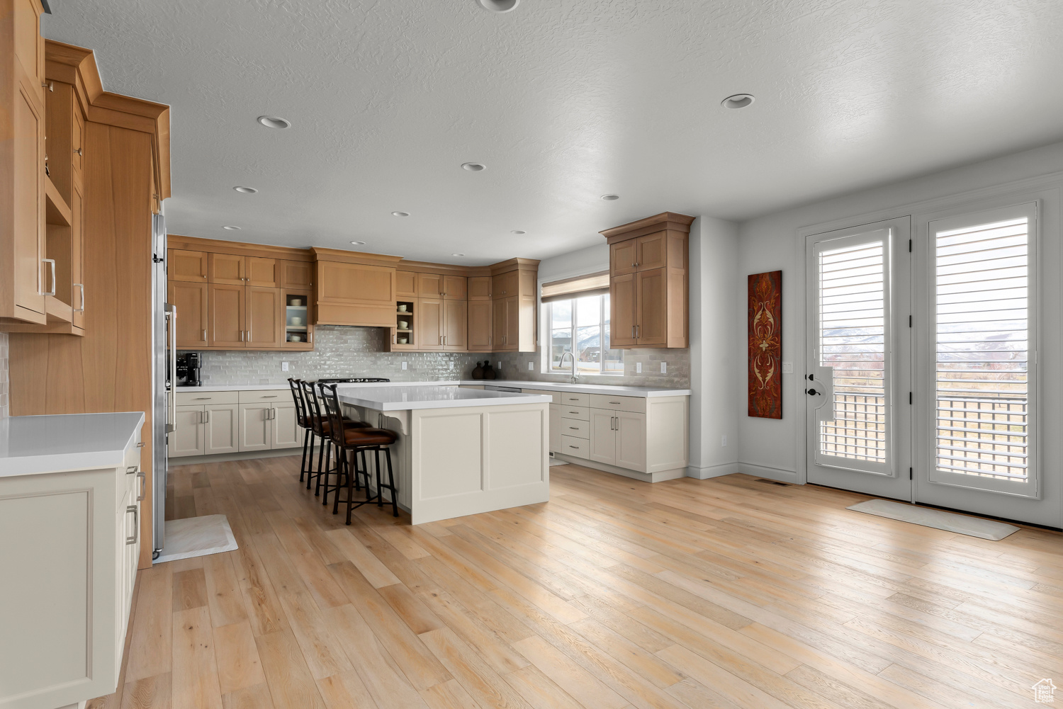 Kitchen with a large island, light hardwood / wood-style floors, tasteful tile backsplash, premium range hood, and built-in appliances. Double Oven, walk-in pantry.