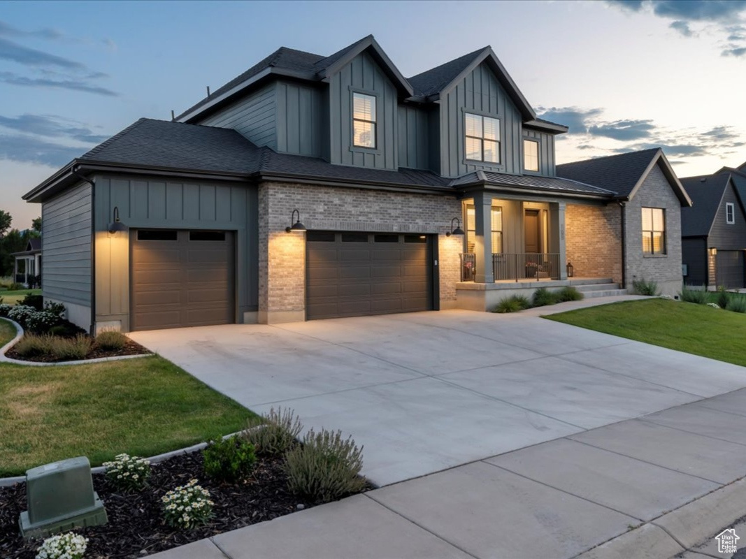 View of front of home with a 3 car garage, covered porch and a lawn