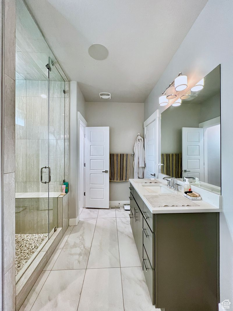 Bathroom with dual vanity, tile floors, and a shower with shower door