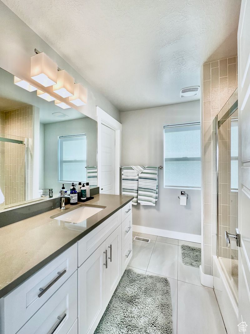Bathroom featuring a textured ceiling, shower / bath combination with glass door, vanity, and tile flooring