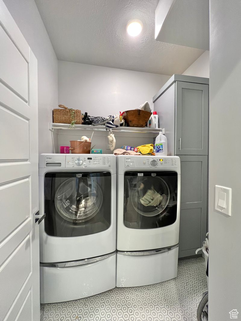 Clothes washing area with independent washer and dryer, a textured ceiling, and light tile flooring