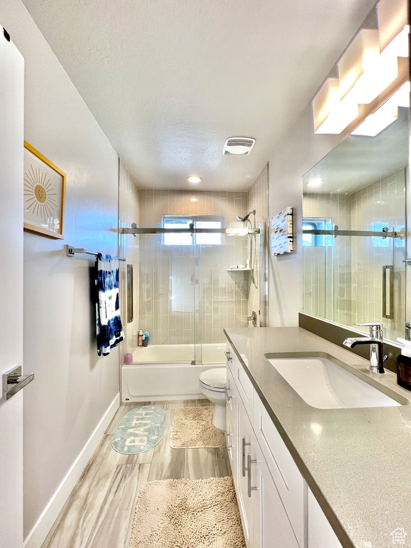 Full bathroom featuring enclosed tub / shower combo, toilet, a textured ceiling, and large vanity
