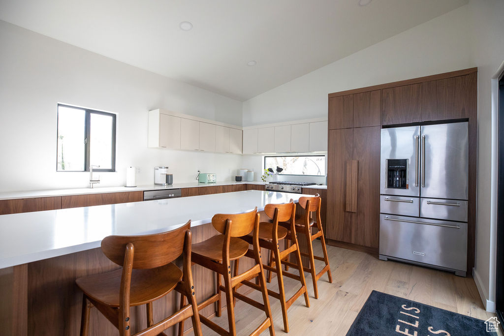 Kitchen with appliances with stainless steel finishes, vaulted ceiling, light hardwood / wood-style floors, white cabinetry, and a kitchen breakfast bar