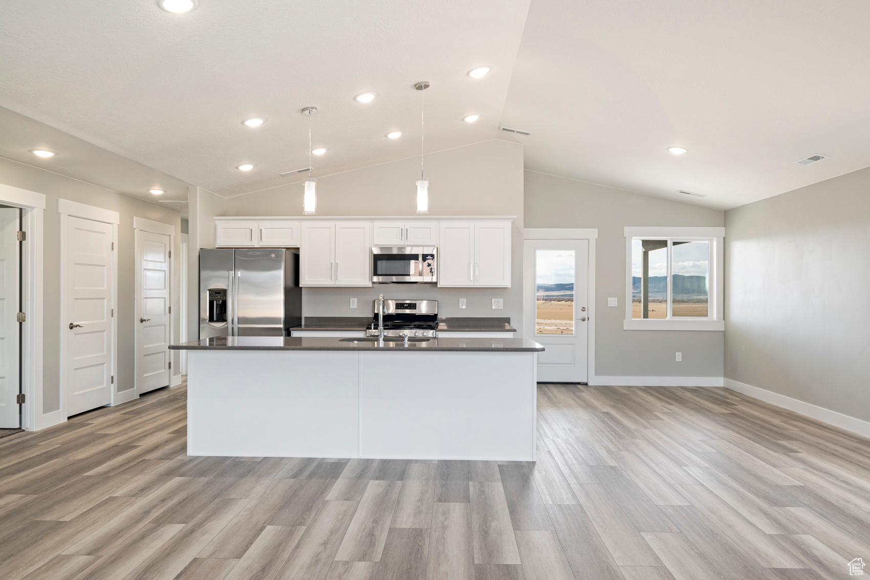 Kitchen featuring white cabinets, light hardwood / wood-style flooring, stainless steel appliances, vaulted ceiling, and an island with sink