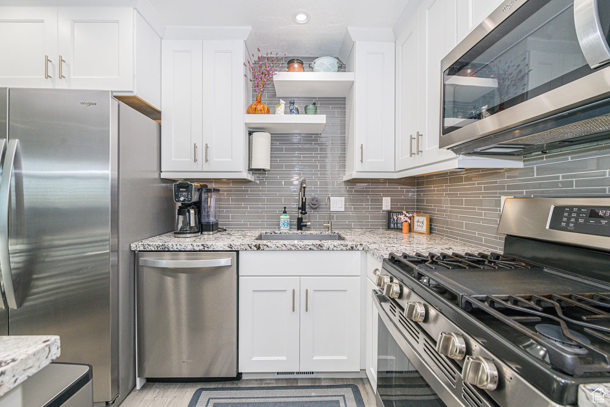 Kitchen featuring white cabinetry, appliances with stainless steel finishes, sink, light stone counters, and tasteful backsplash