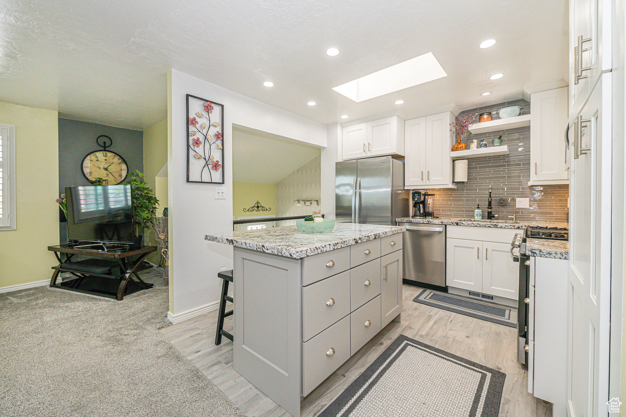Kitchen with light colored carpet, appliances with stainless steel finishes, white cabinets, a skylight, and a center island