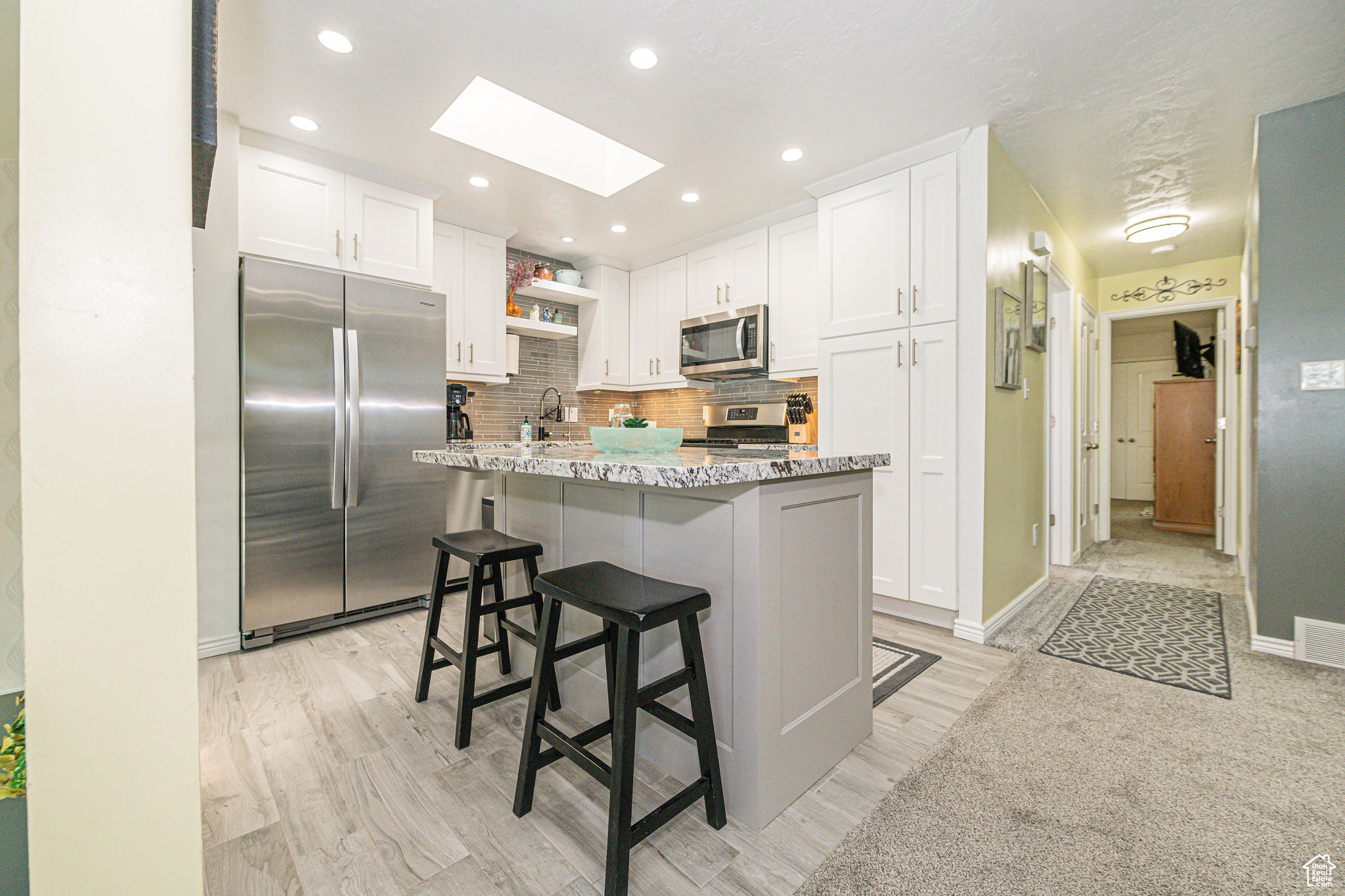 Kitchen with a skylight, tasteful backsplash, stainless steel appliances, and white cabinets