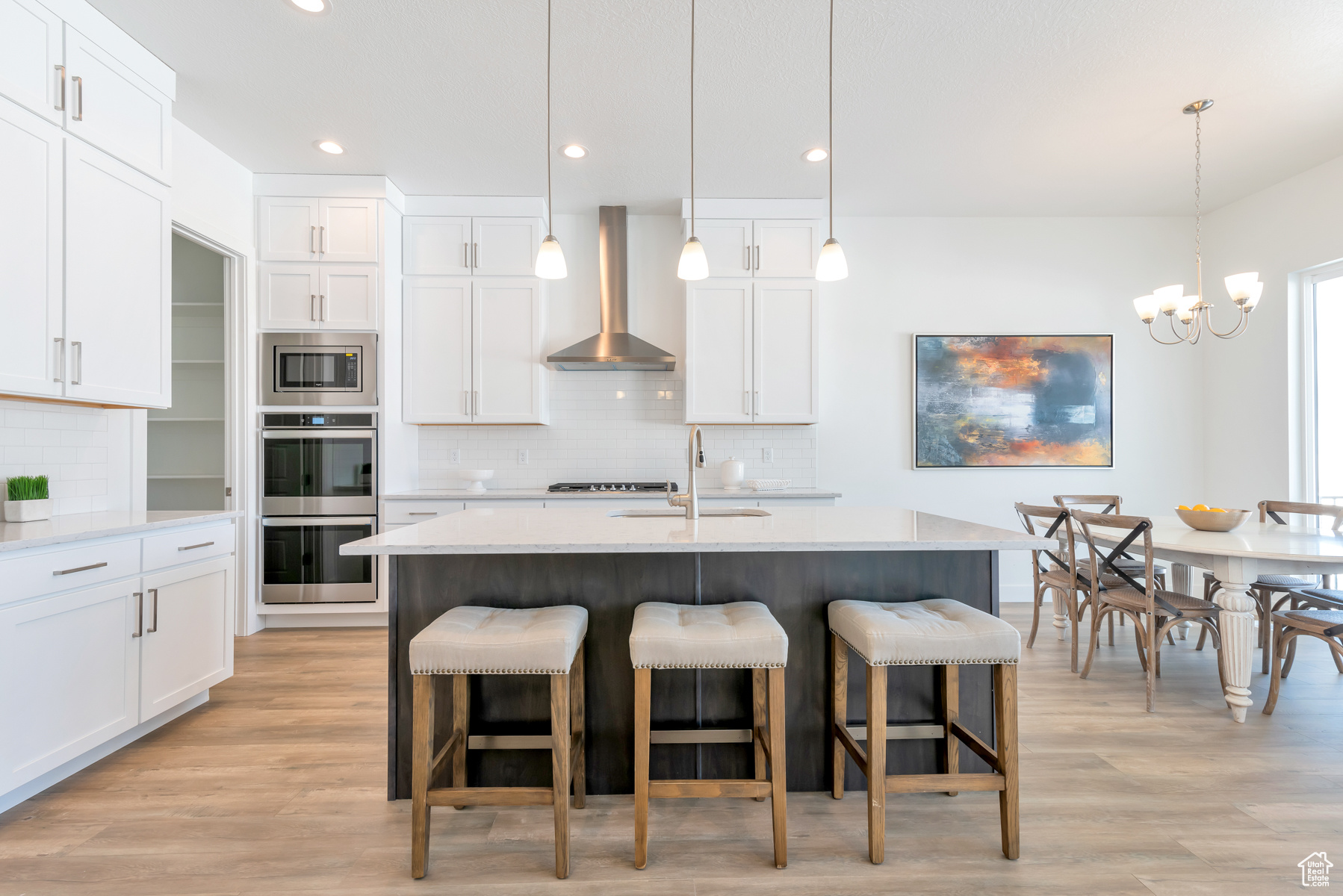 Kitchen featuring backsplash, light wood-type flooring, pendant lighting, and wall chimney range hood