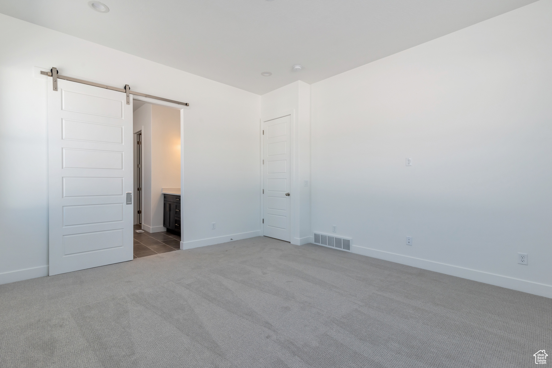 Unfurnished bedroom with a barn door, connected bathroom, and dark carpet