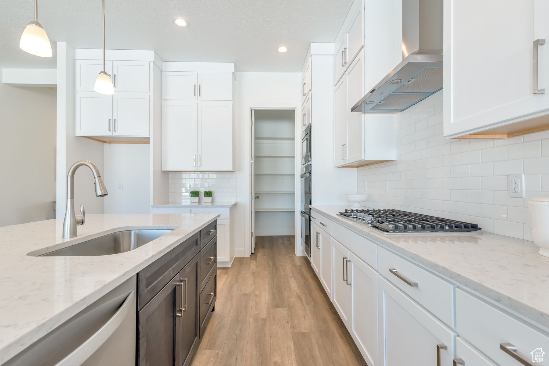 Kitchen with hood, hanging light fixtures, white cabinets, light wood-type flooring, and tasteful backsplash