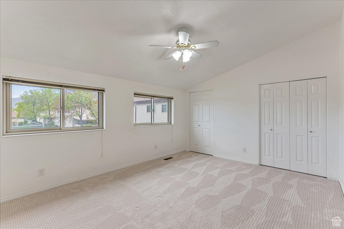 Unfurnished bedroom featuring light colored carpet, ceiling fan, and vaulted ceiling