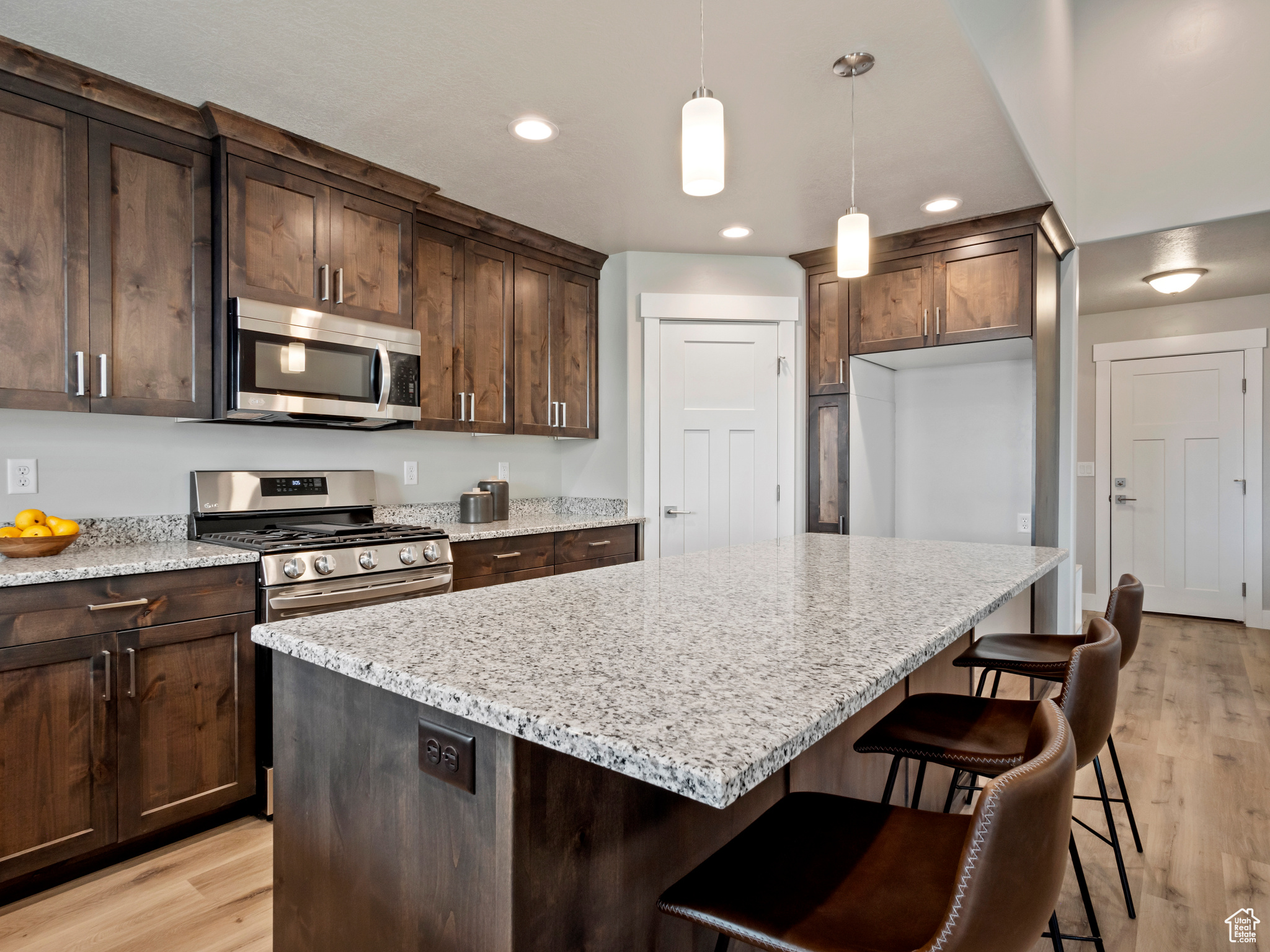 Kitchen featuring pendant lighting, appliances with stainless steel finishes, a breakfast bar area, light stone counters, and light hardwood / wood-style floors