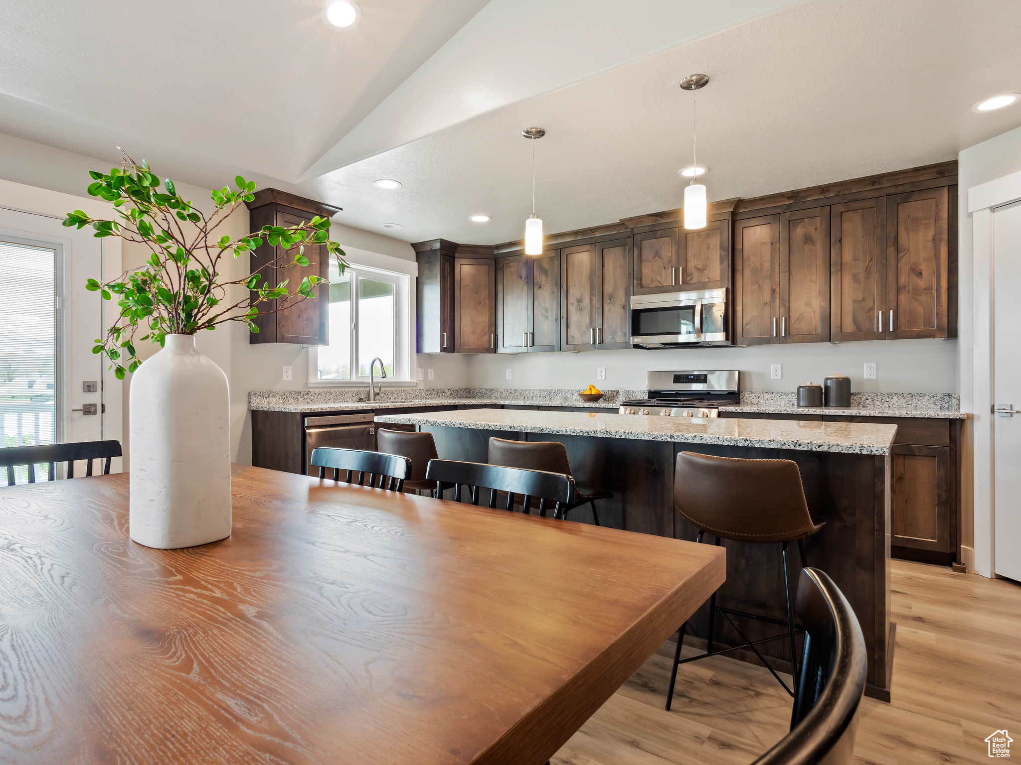 Kitchen featuring light stone countertops, decorative light fixtures, light hardwood / wood-style flooring, stainless steel appliances, and a center island