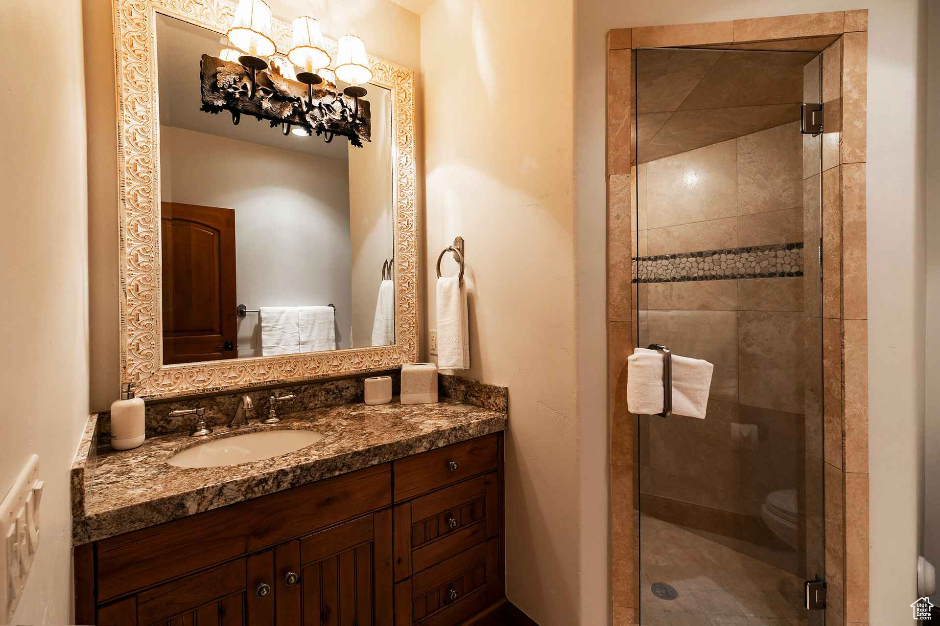 Bathroom with a shower with shower door, toilet, vanity with extensive cabinet space, and a notable chandelier