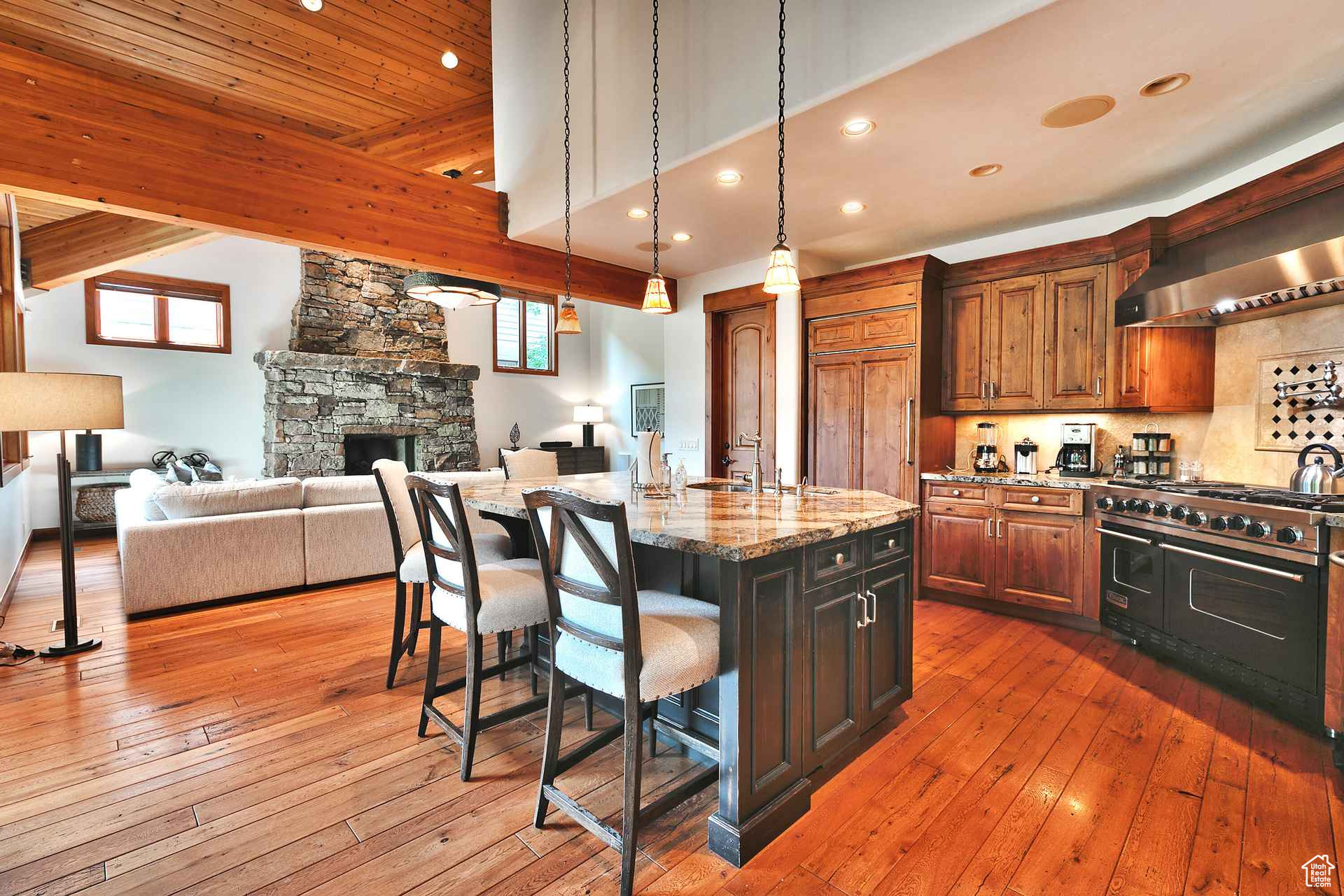 Kitchen featuring a fireplace, a breakfast bar, double oven range, wood-type flooring, and light stone countertops