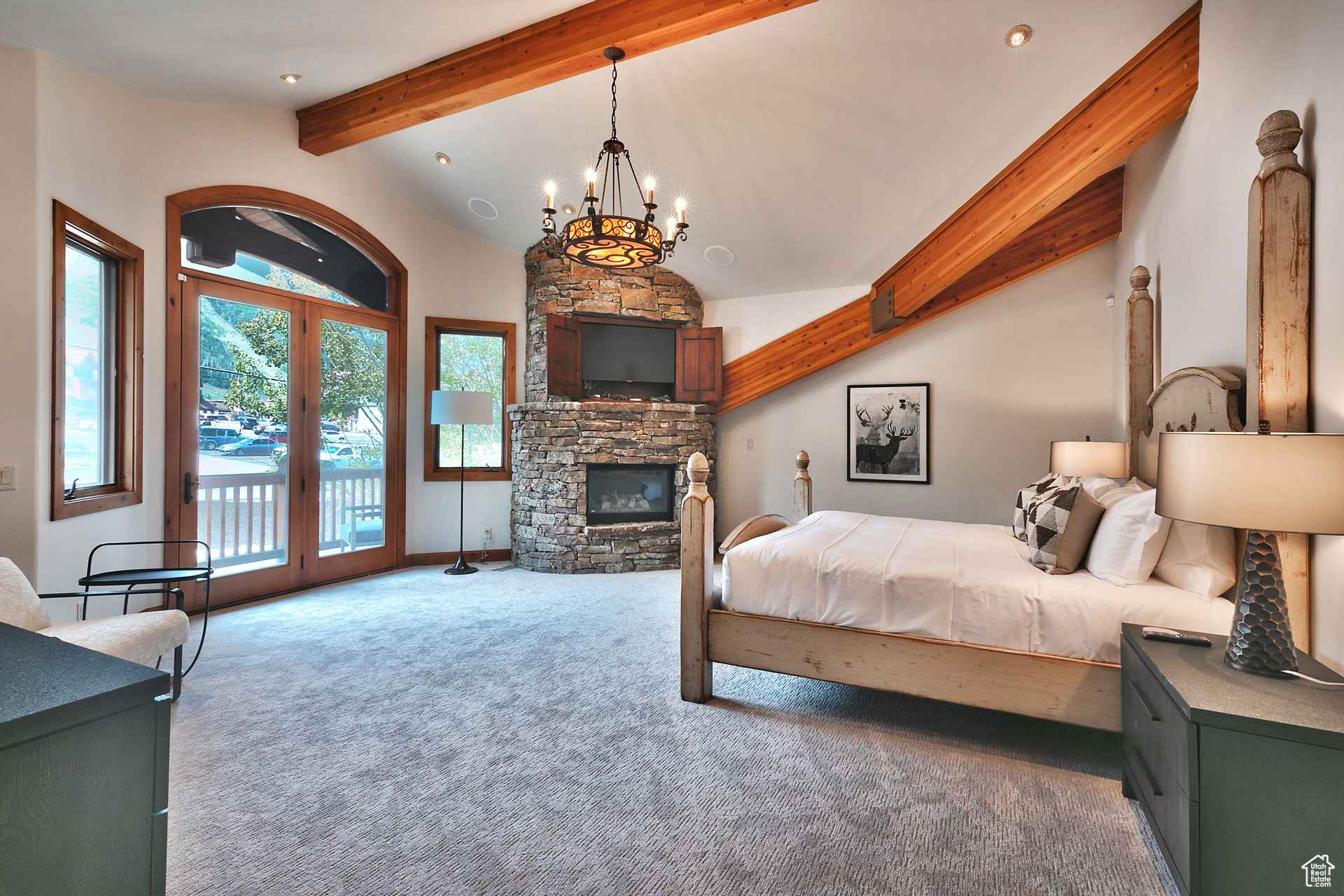 Bedroom featuring a stone fireplace, lofted ceiling with beams, carpet flooring, access to outside, and an inviting chandelier