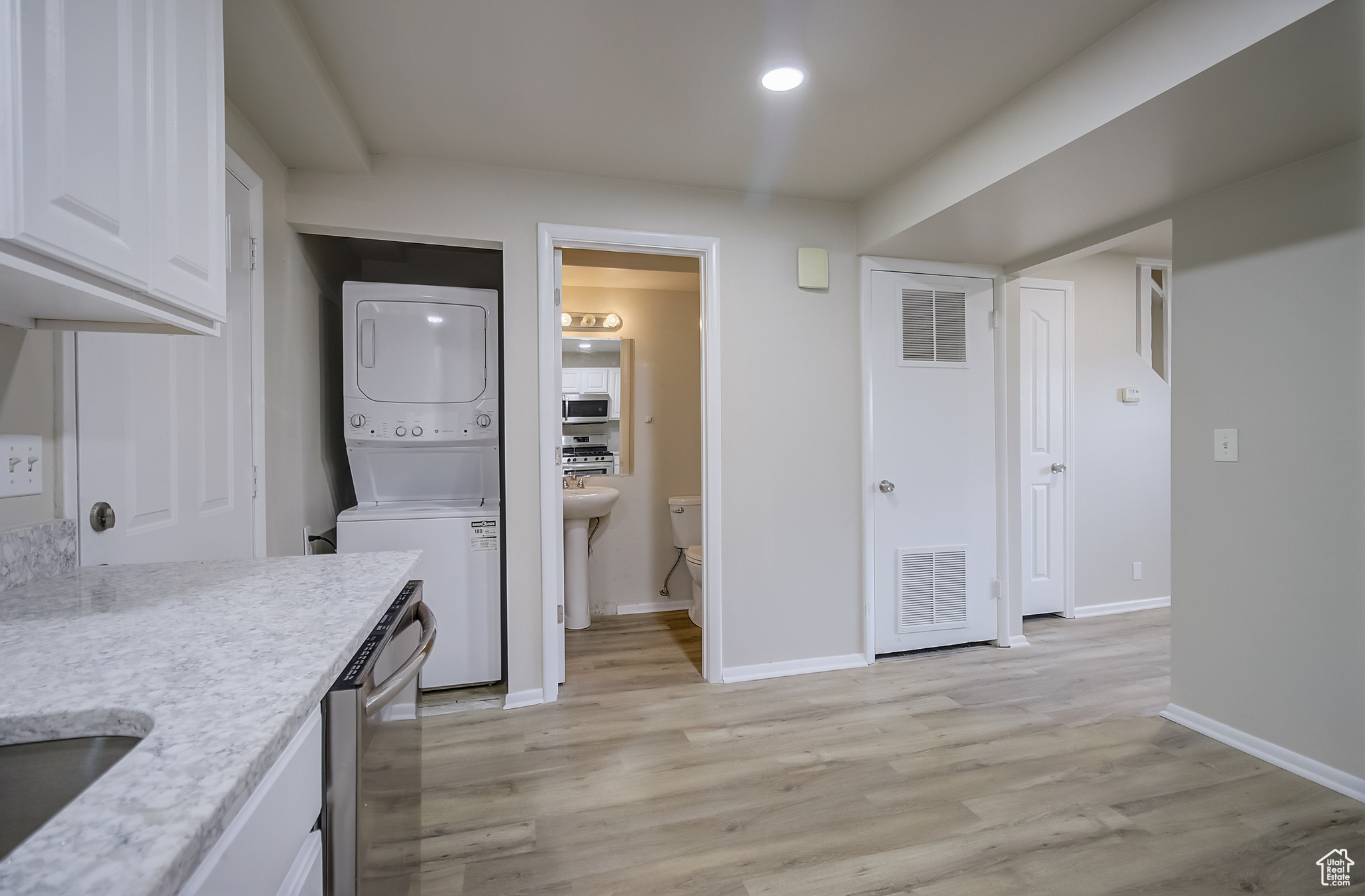 Kitchen featuring white cabinets, light hardwood / wood-style flooring, stainless steel appliances, and stacked washer and dryer