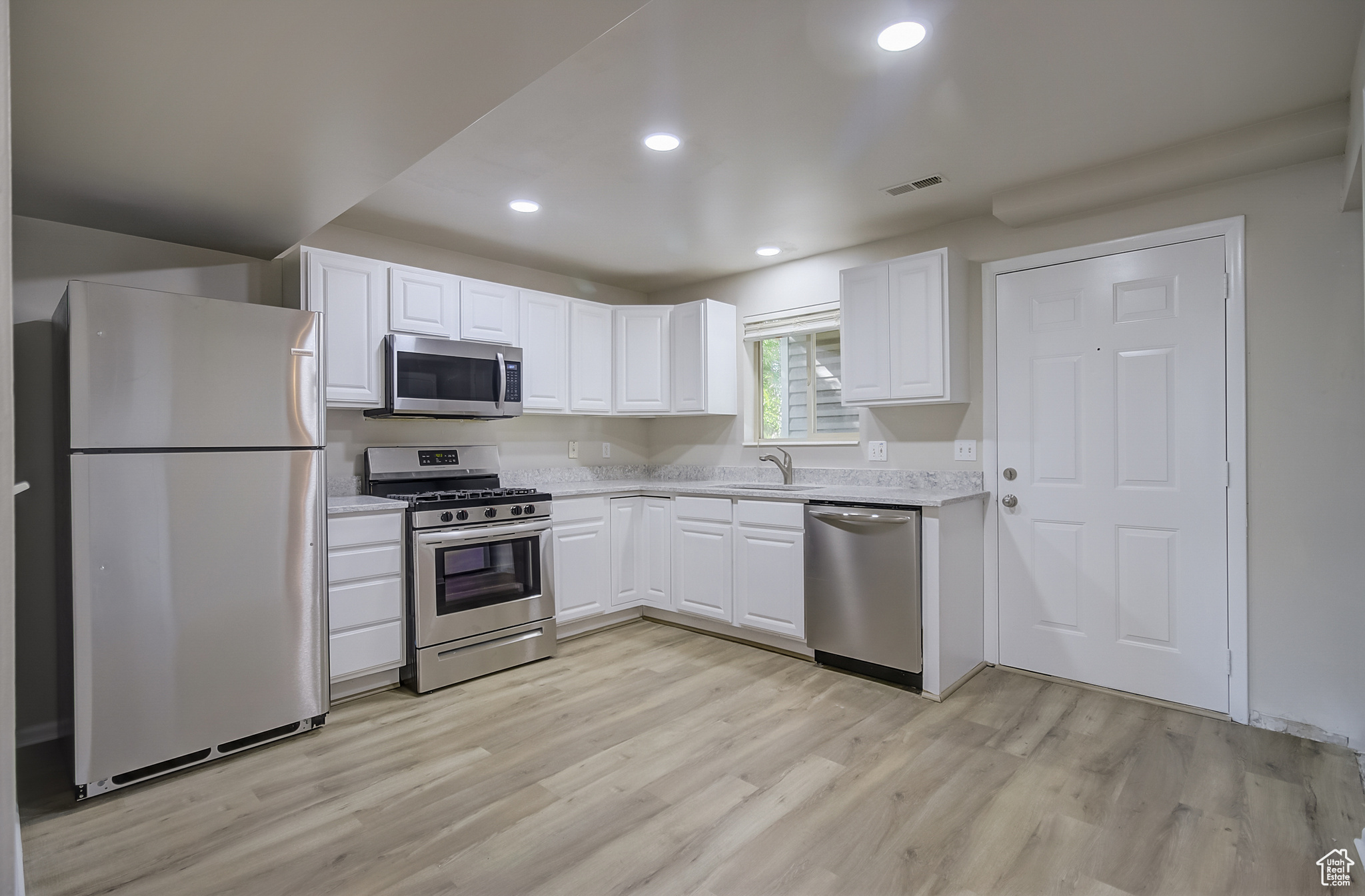 Kitchen with white cabinets, sink, stainless steel appliances, and light hardwood / wood-style floors