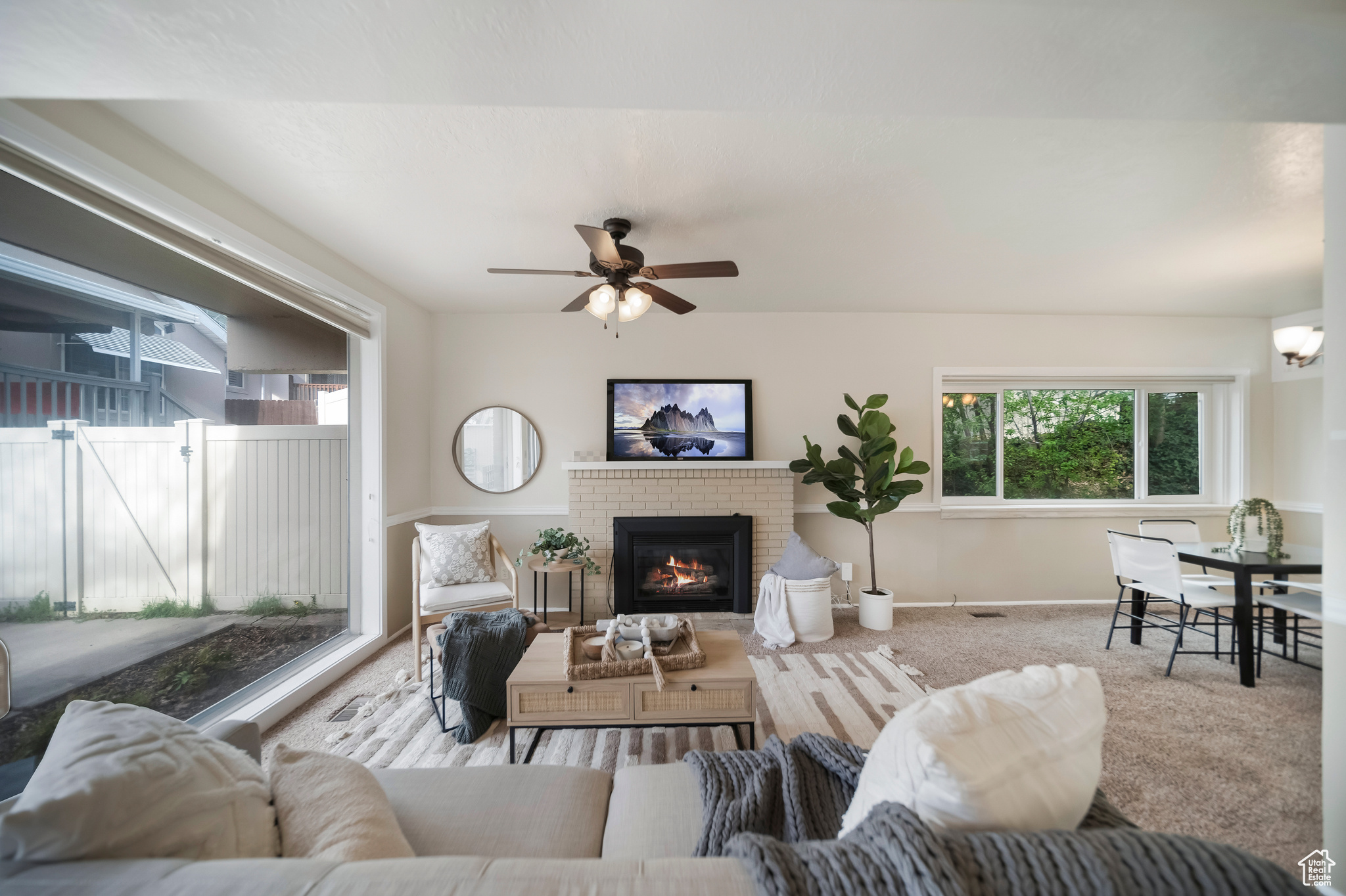Carpeted living room featuring ceiling fan and a brick fireplace
