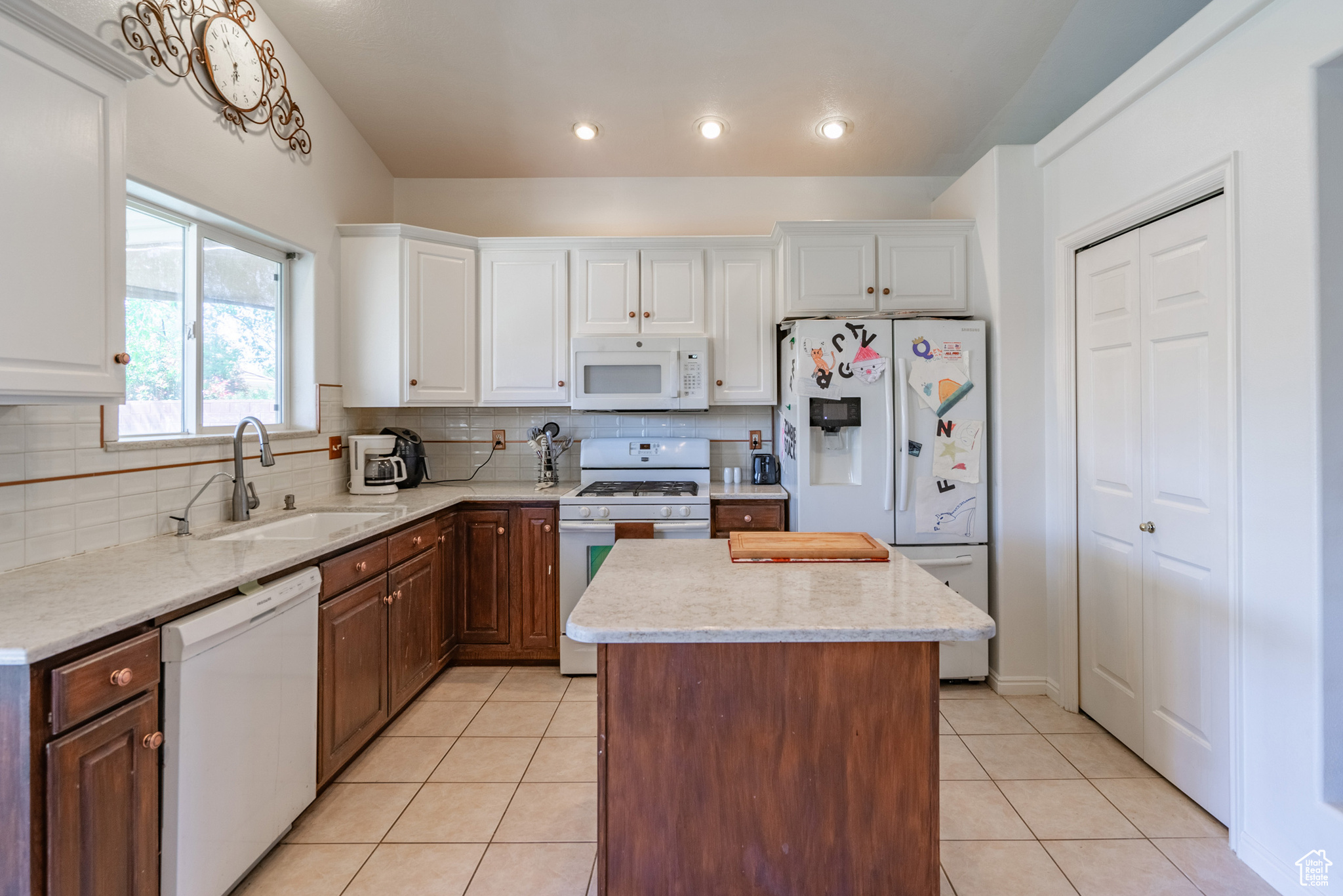 Kitchen featuring a center island, white cabinets, dark brown cabinets, and white appliances
