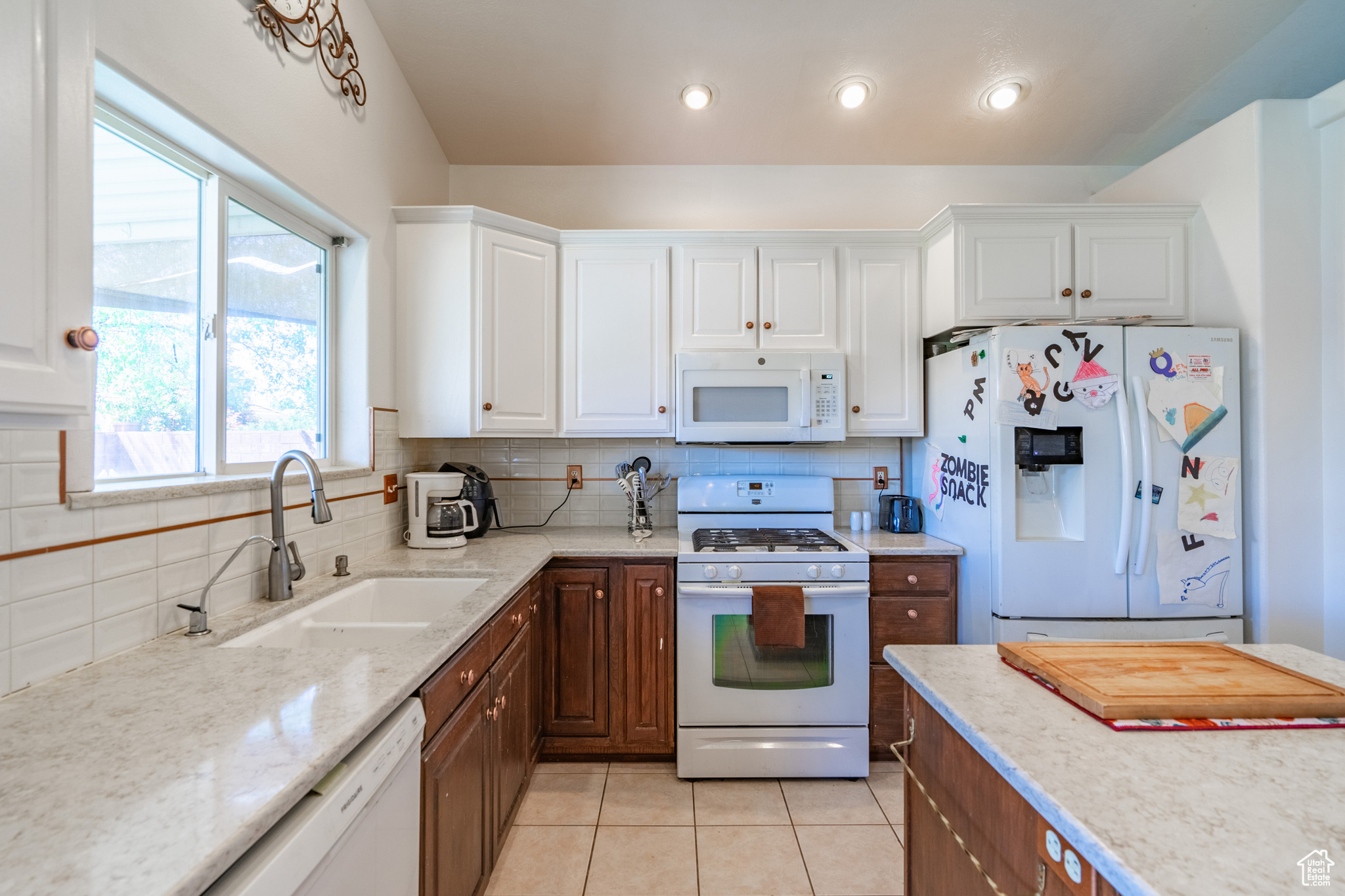 Kitchen with backsplash, white appliances, white cabinetry, sink, and light tile floors