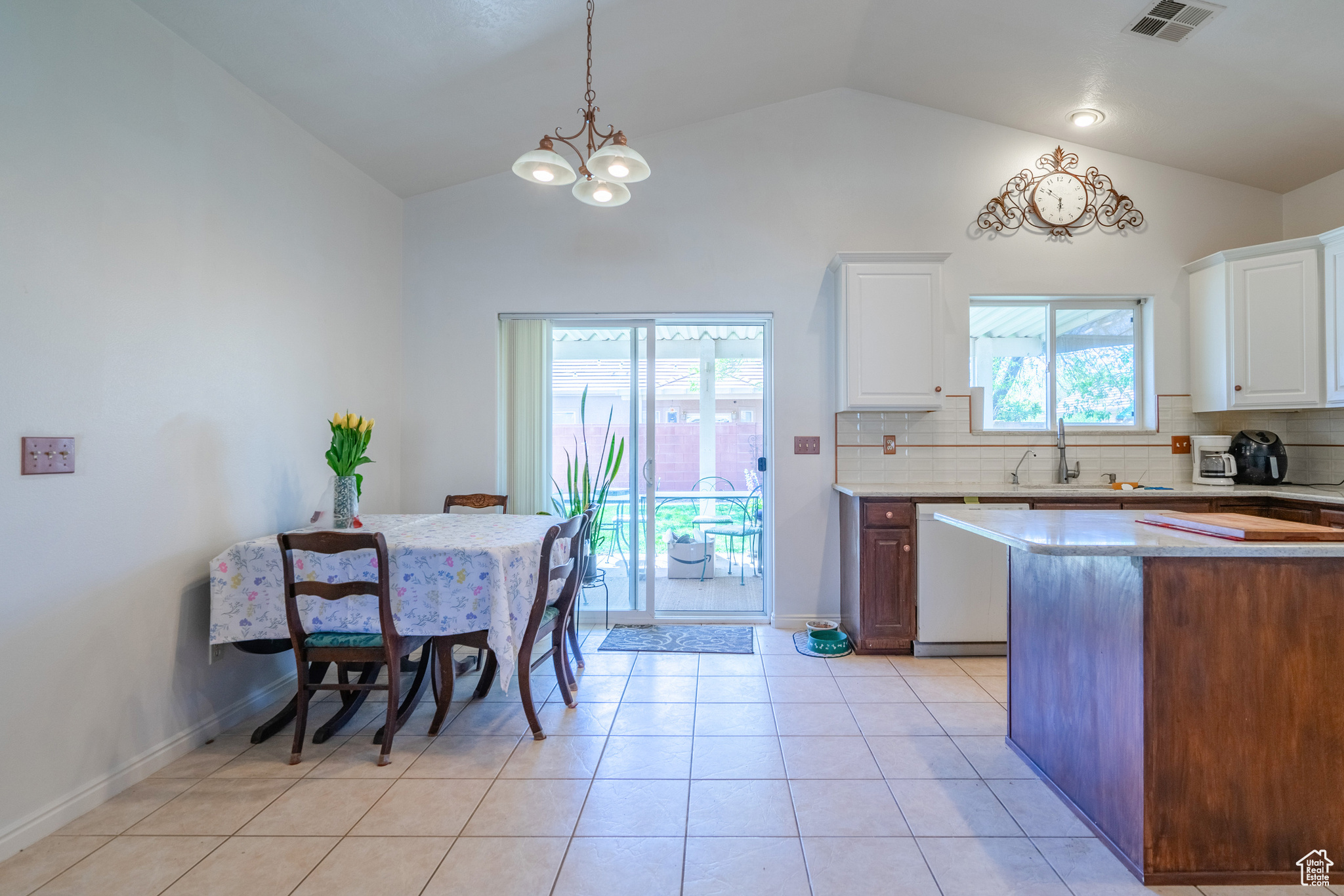 Kitchen featuring white dishwasher, light tile flooring, tasteful backsplash, white cabinetry, and pendant lighting