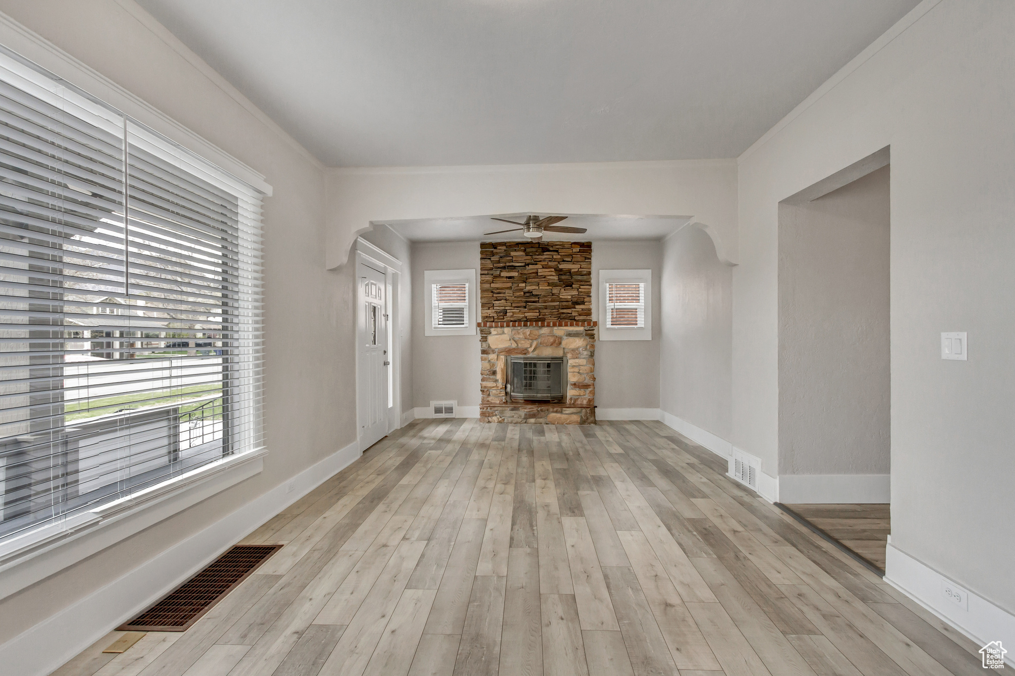 Unfurnished living room with light hardwood / wood-style flooring, ceiling fan, and a stone fireplace