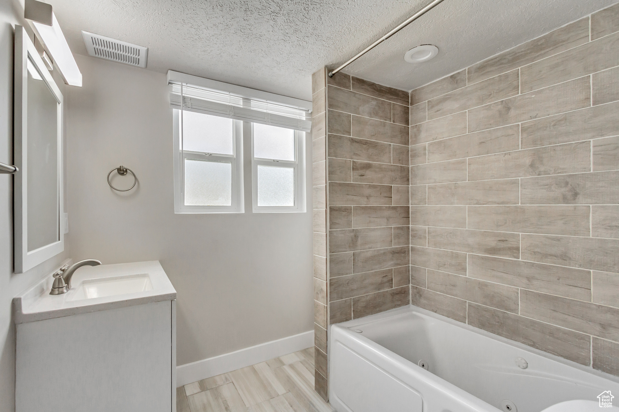 Bathroom with tiled shower / bath combo, vanity, and a textured ceiling