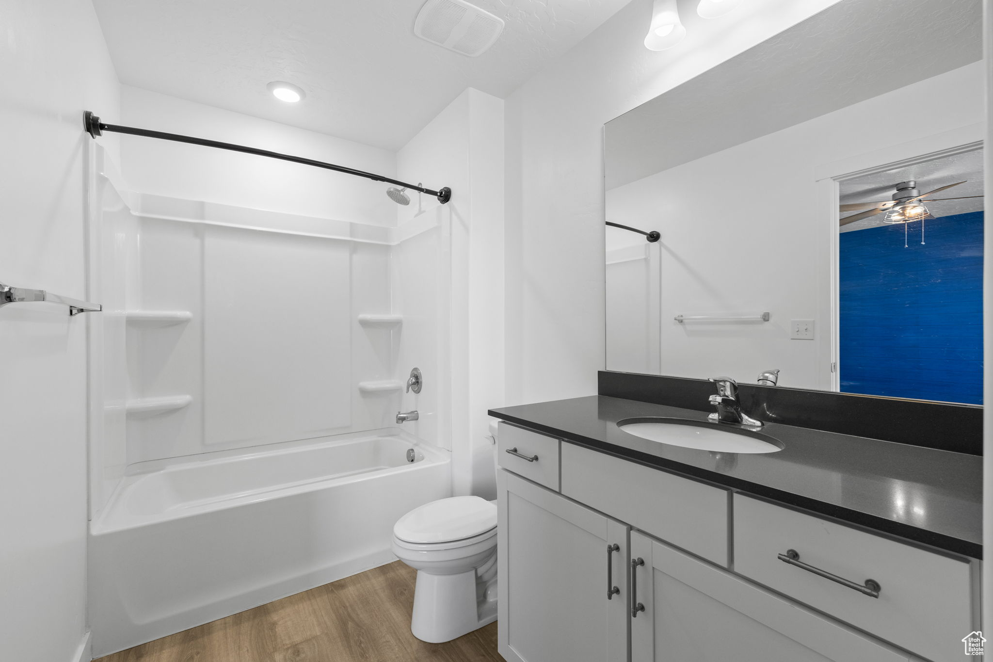 Full bathroom featuring oversized vanity, ceiling fan, shower / bathtub combination, toilet, and hardwood / wood-style floors